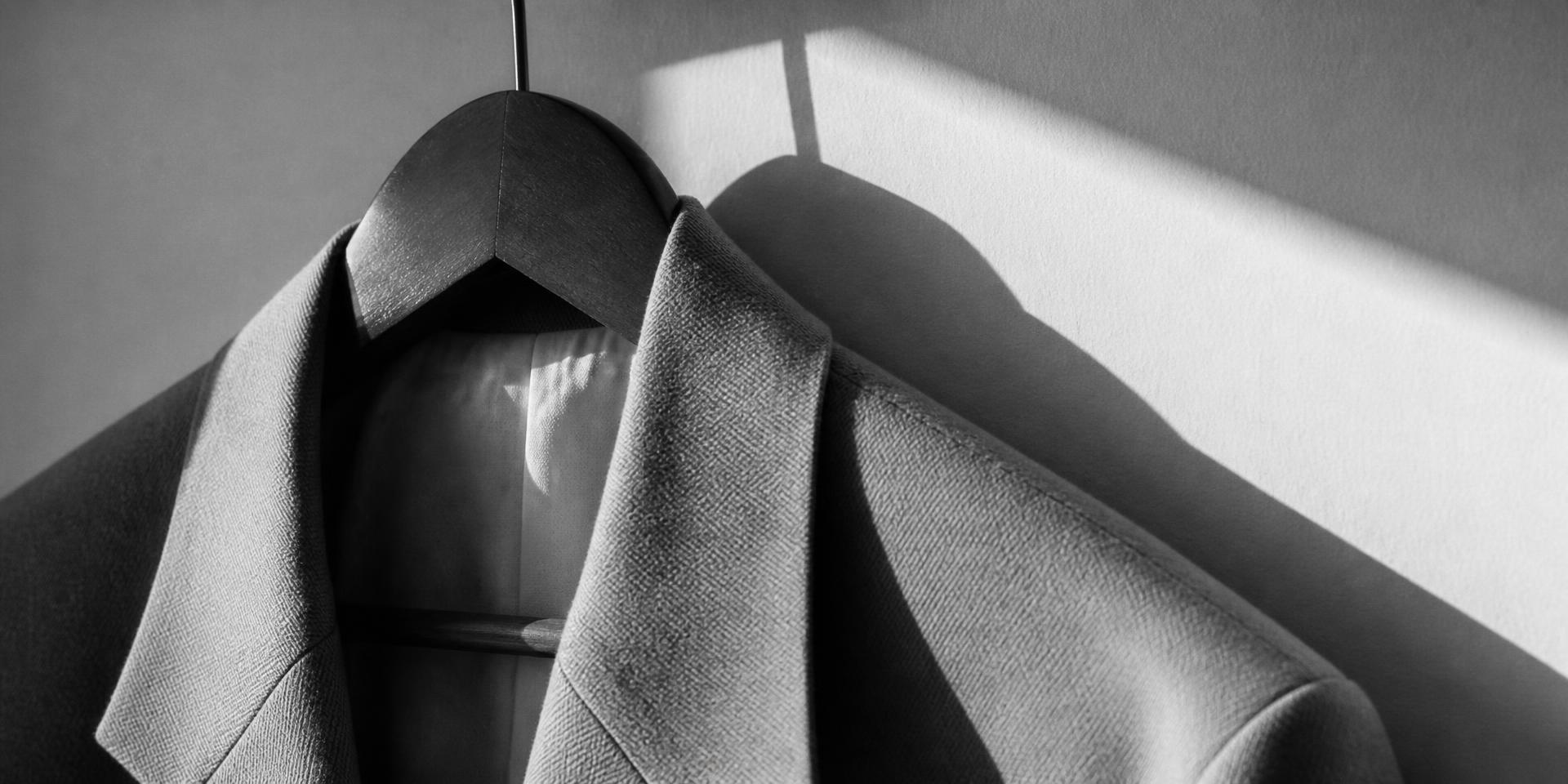 Close detail of a tailored garment on a wooden hanger in a minimal showroom